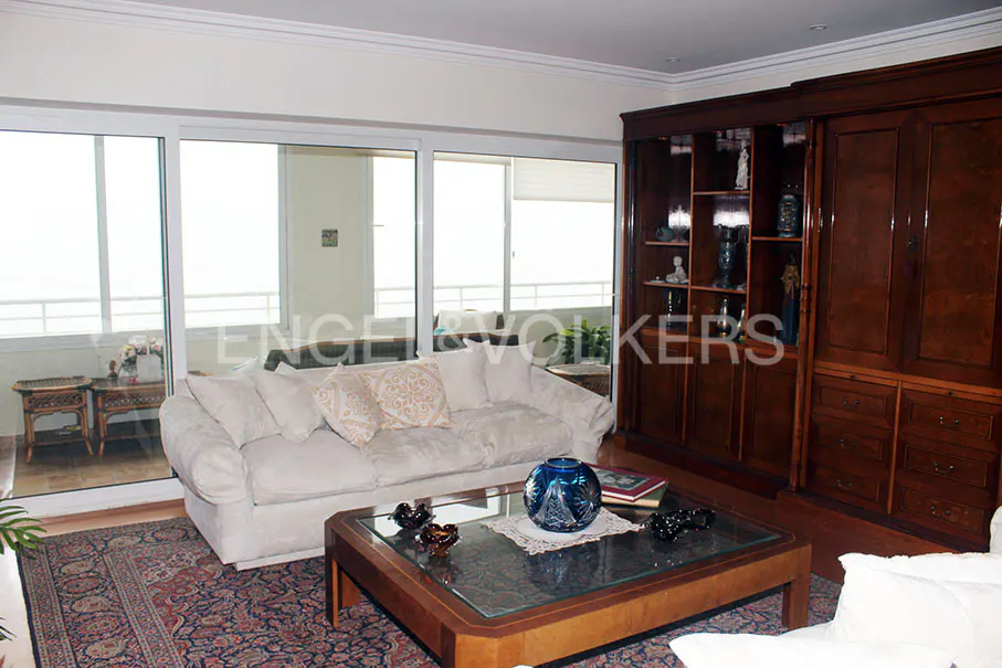 Living room with a white sofa, glass coffee table, and a dark wood cabinet. Large windows offer a bright view.