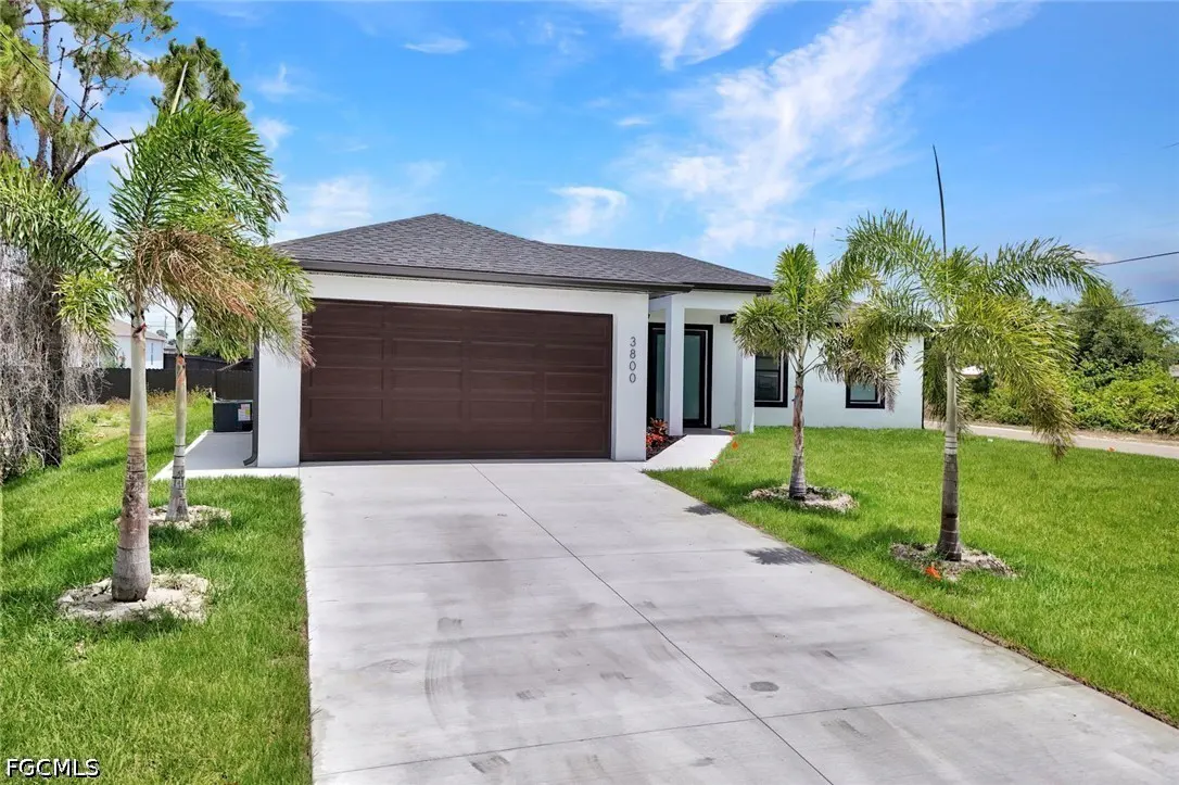 A modern, single-story white house with a brown garage door, palm trees, and a concrete driveway under a blue sky.