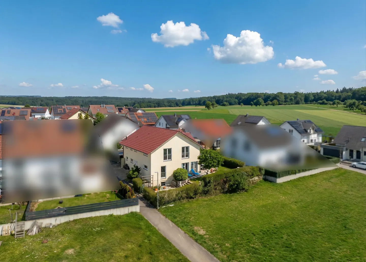 Aerial view of a two-story beige house with a red roof, green lawn, and blue sky with white clouds.