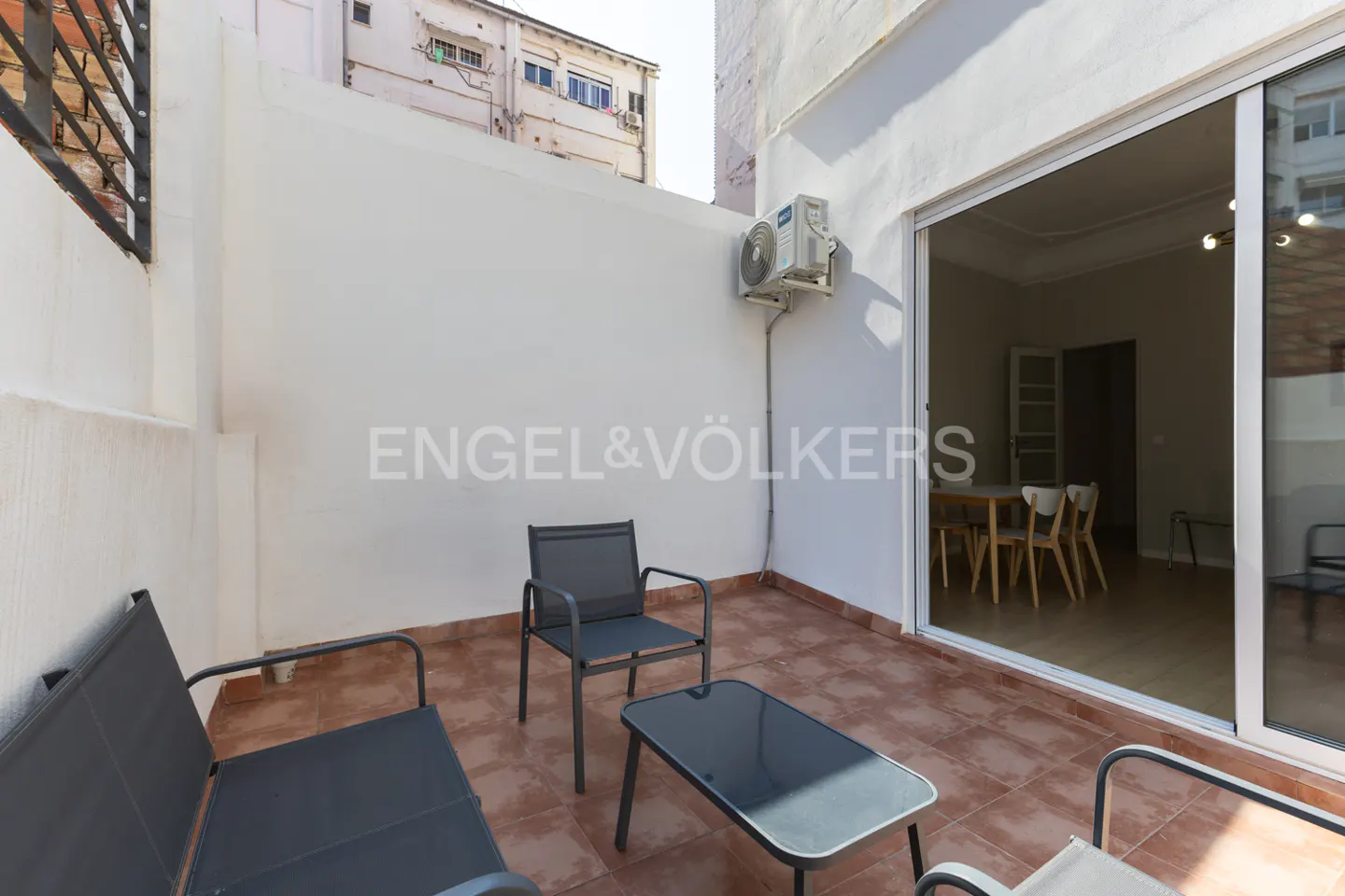 Outdoor patio with gray furniture, a table, and a view into a dining room through a sliding glass door. The patio has red tile flooring.