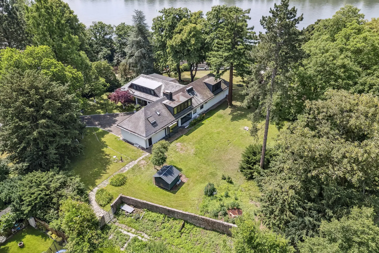 Aerial view of a white house with a gray roof surrounded by green trees and grass, near a river.
