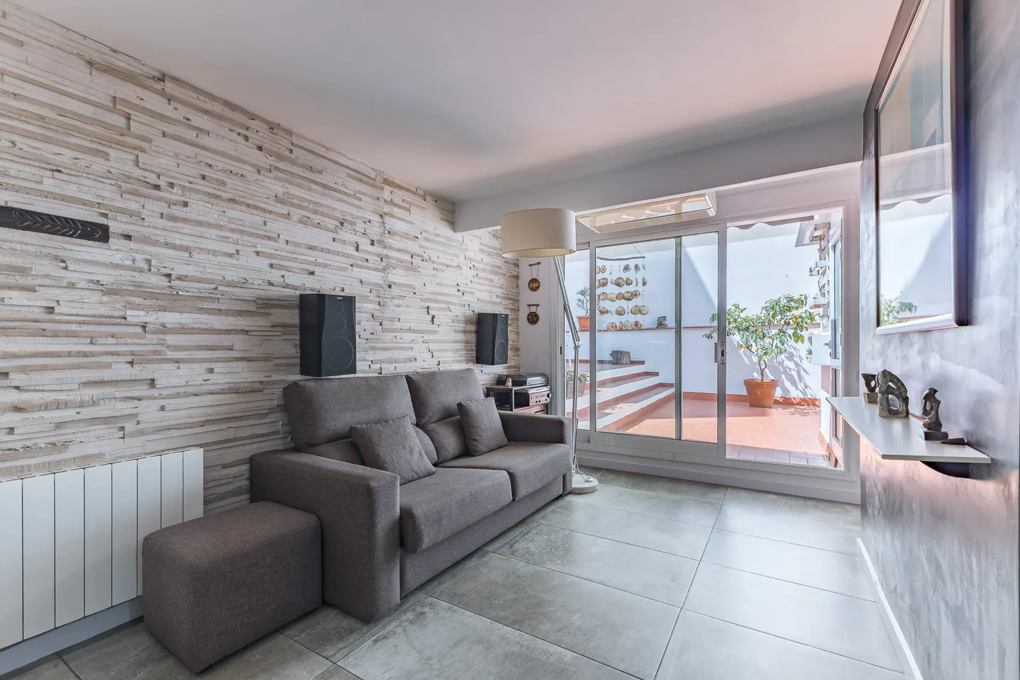Living room with gray sofa, stone accent wall, and sliding glass doors to a patio with a potted tree.