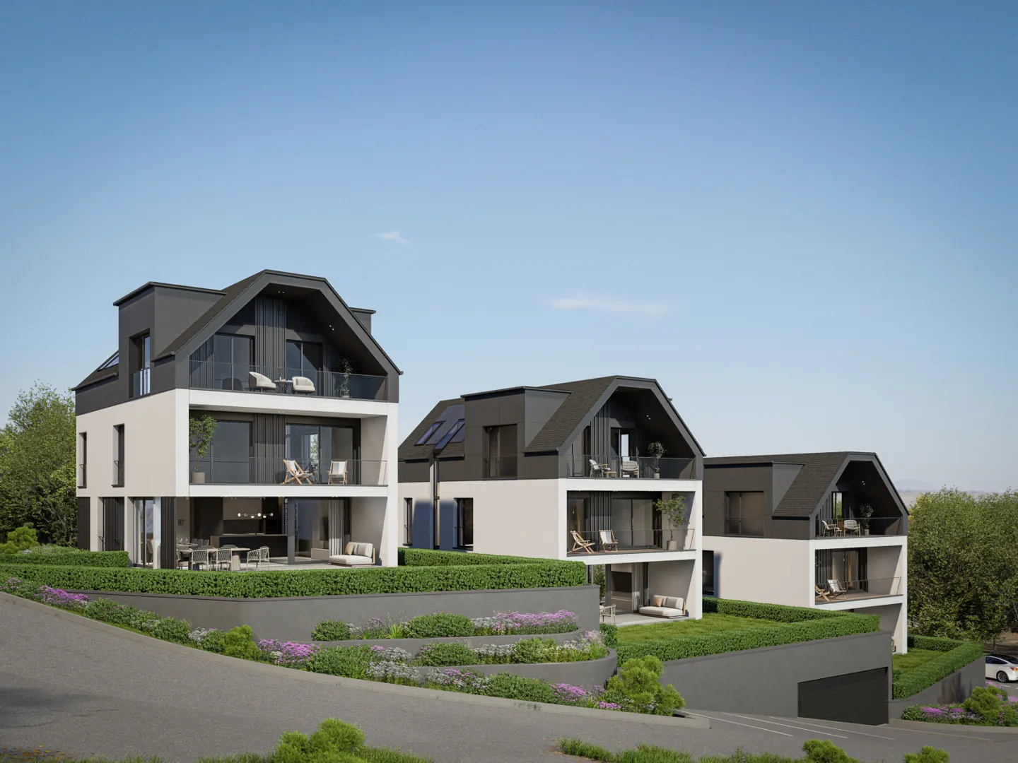 Three modern, white townhouses with dark gray roofs and balconies sit on a terraced, landscaped hill under a blue sky.