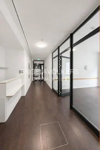 Modern office hallway with dark wood floors, white walls, and glass-walled rooms under bright recessed lighting.