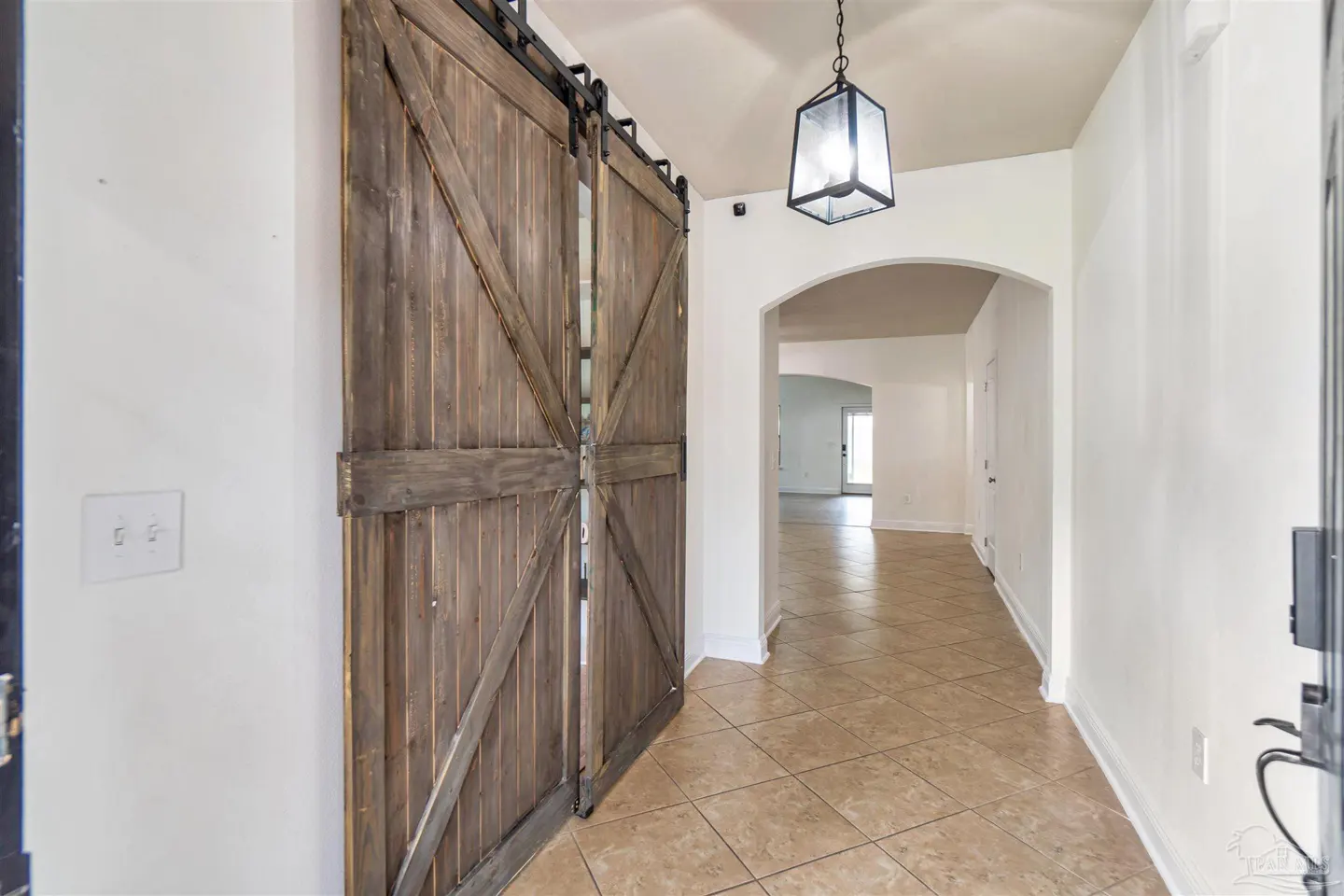 Entryway with tan tile floor, white walls, and rustic wood barn doors. A hanging lantern light fixture is visible.
