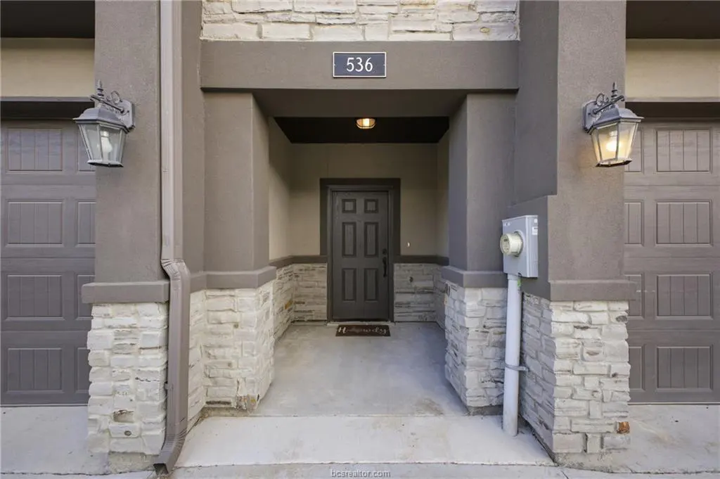 Exterior view of a home's entrance with a gray door, stone accents, and address number 536 above the door. Two garage doors are visible on either side.
