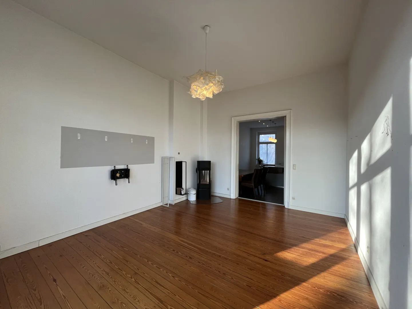 Empty room with wood floors, white walls, and a modern light fixture. A fireplace and TV mount are visible.