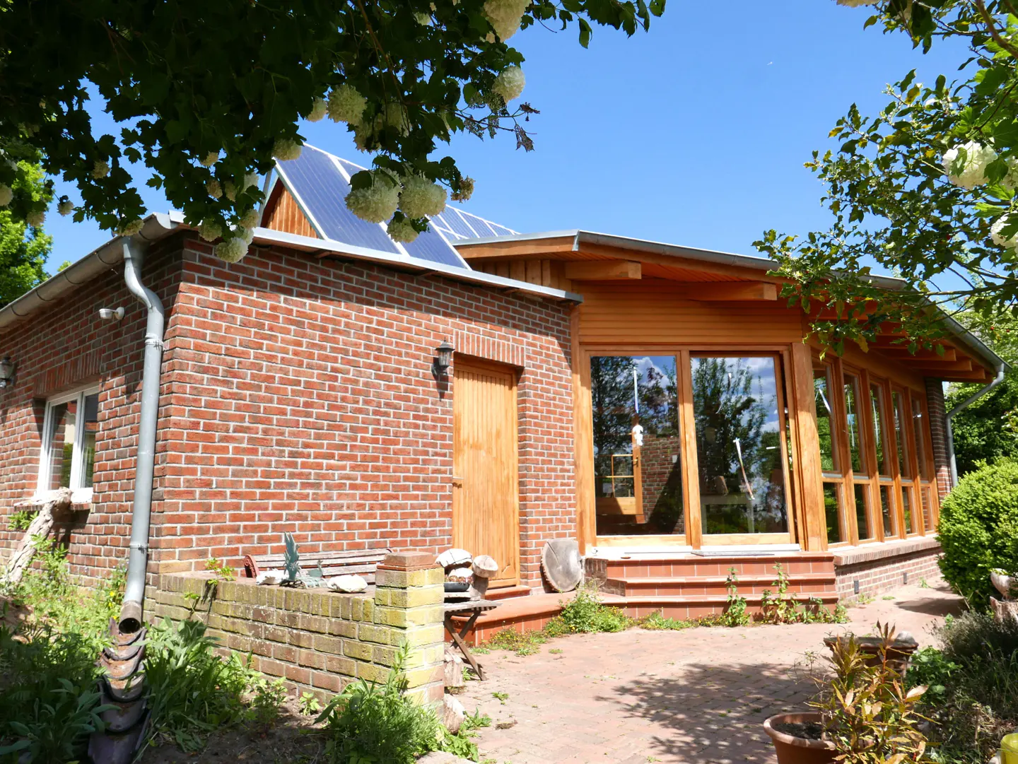 Exterior view of a brick and wood home with solar panels on the roof, surrounded by greenery.