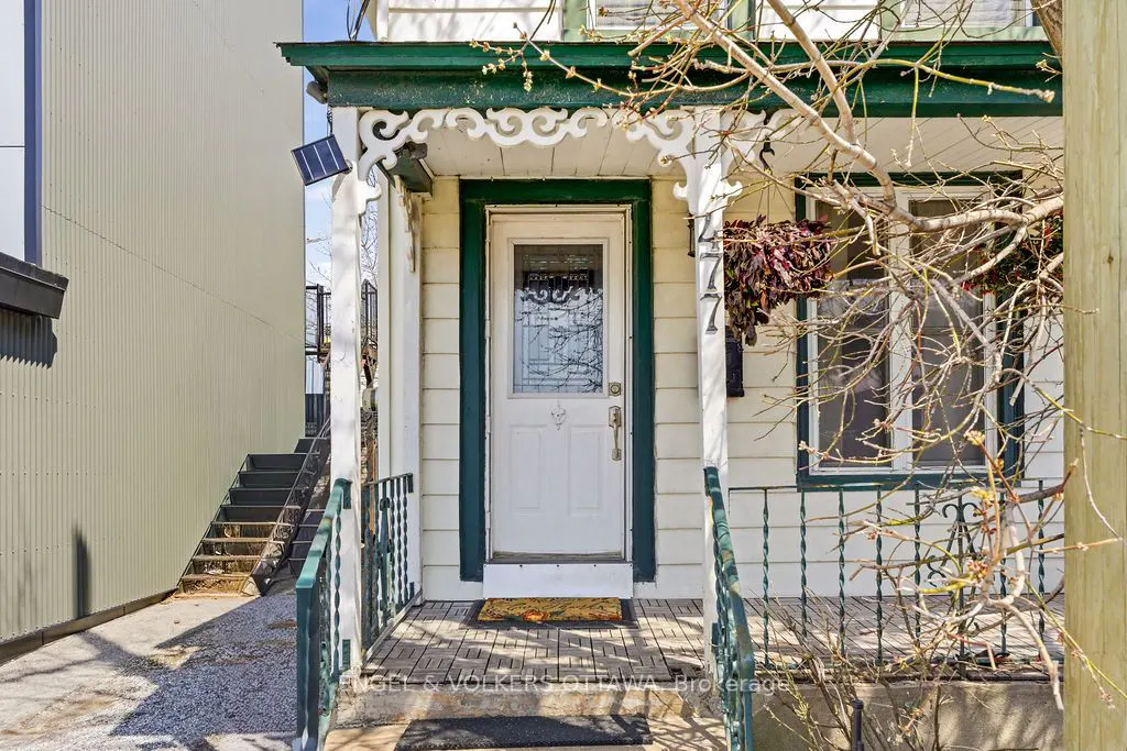 Front view of a white house with green trim, a white door with a decorative glass window, and a small porch with green railings.
