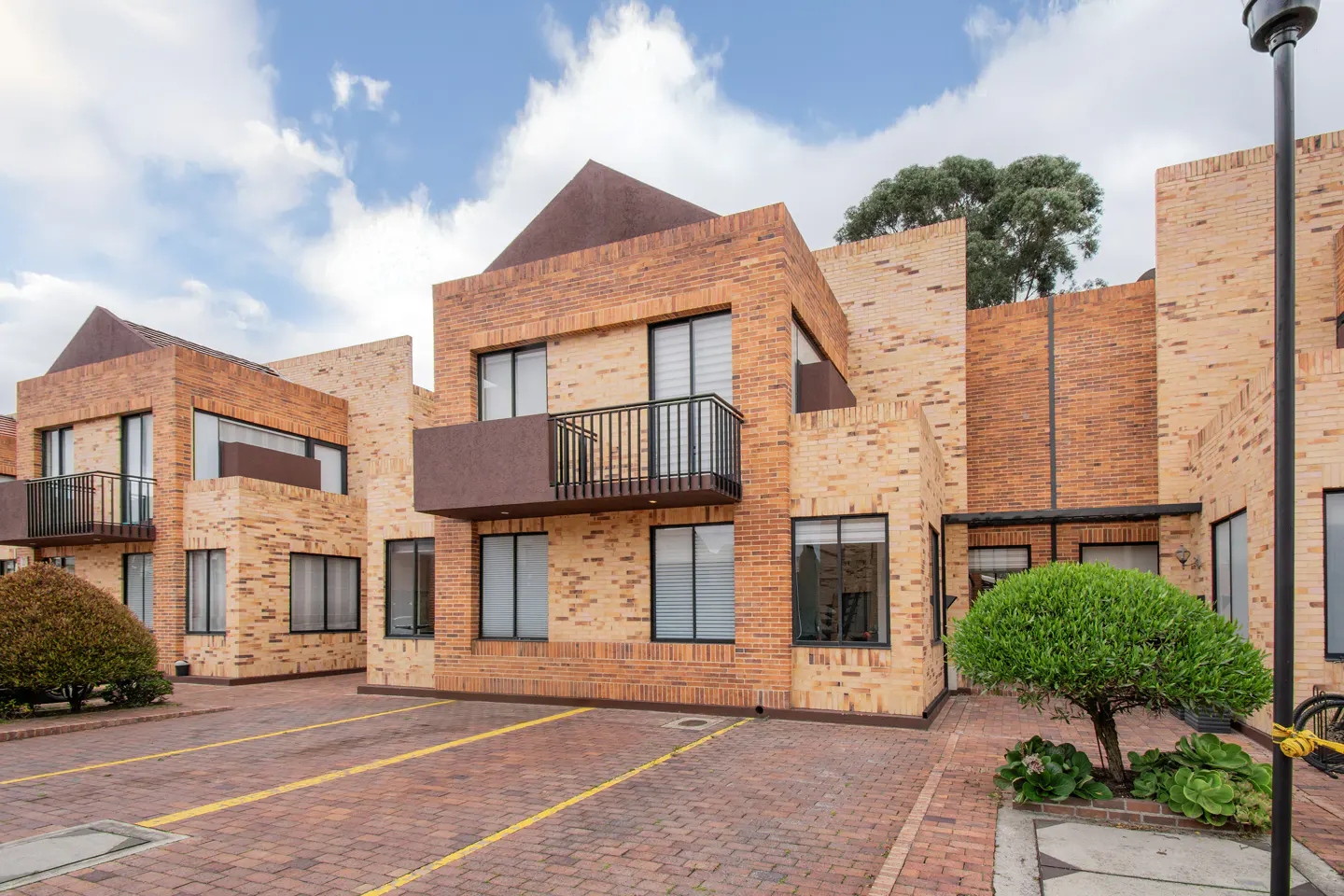 Exterior view of modern brick townhouses with black framed windows and balconies, under a cloudy sky.