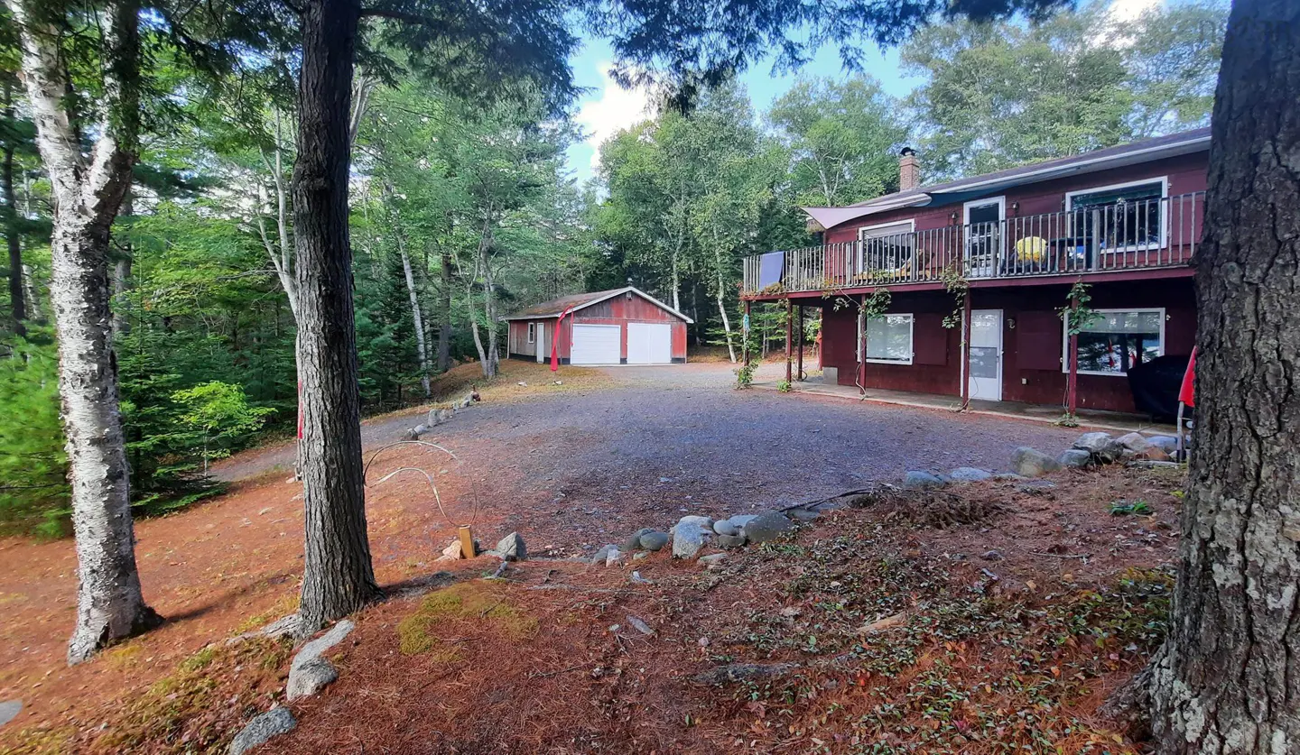 A two-story red house with a balcony and a detached garage surrounded by trees.