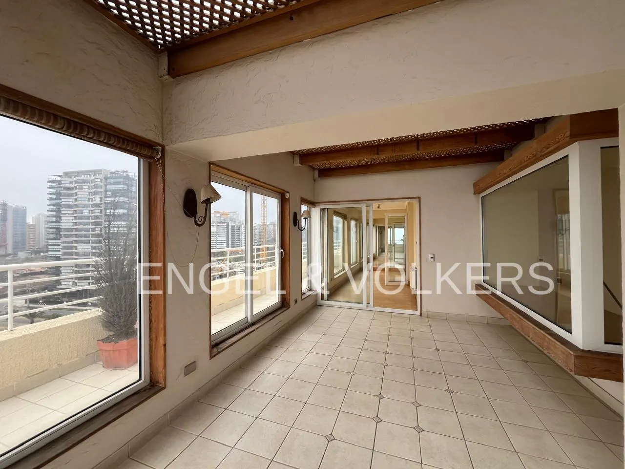 Bright, tiled sunroom with large windows, wooden ceiling beams, and a view of city high-rise buildings.