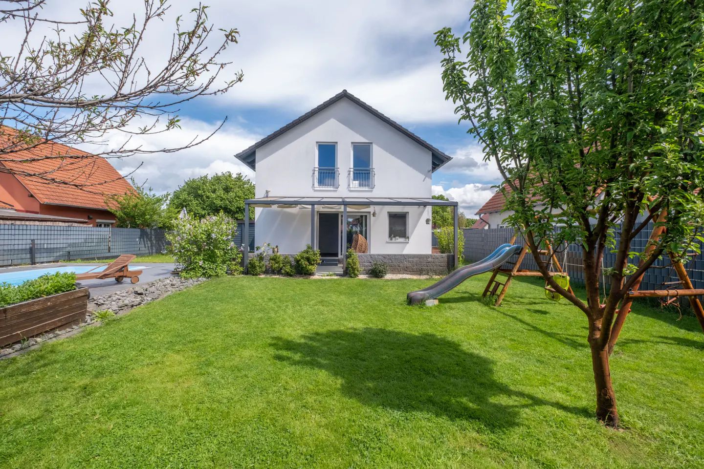 A white two-story house with a green lawn, a slide, and a swing set in the backyard.