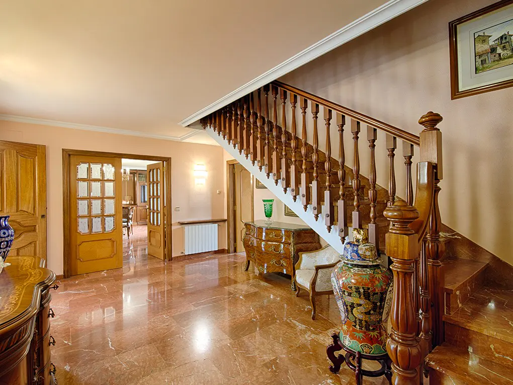 Elegant foyer with marble floors, wooden staircase, and antique furniture. Open doorway leads to a dining room.