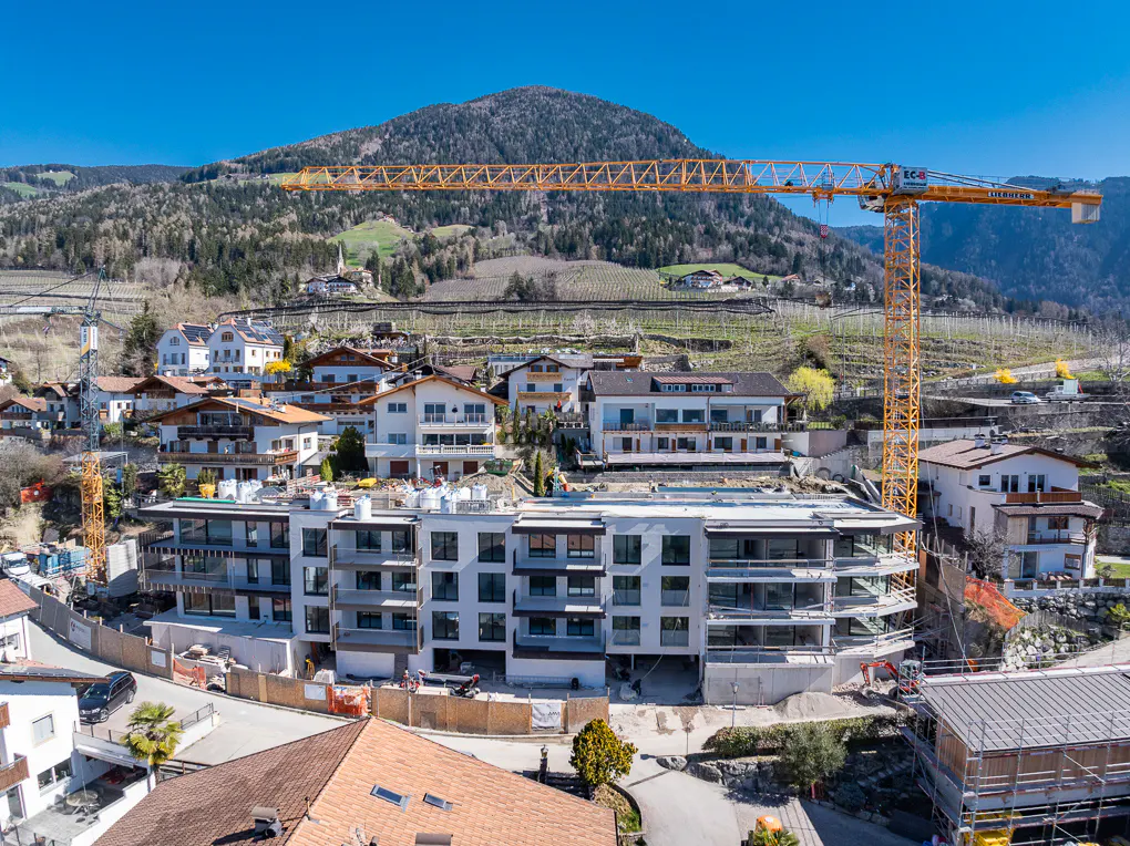 Construction site with a crane in a hillside town. A new building is being constructed with a yellow crane in the background.
