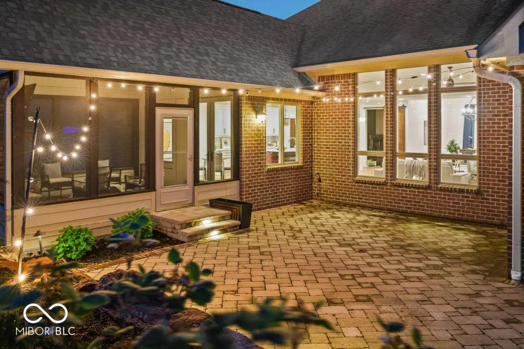 Brick patio with string lights at dusk. Screened porch and large windows show interior details.