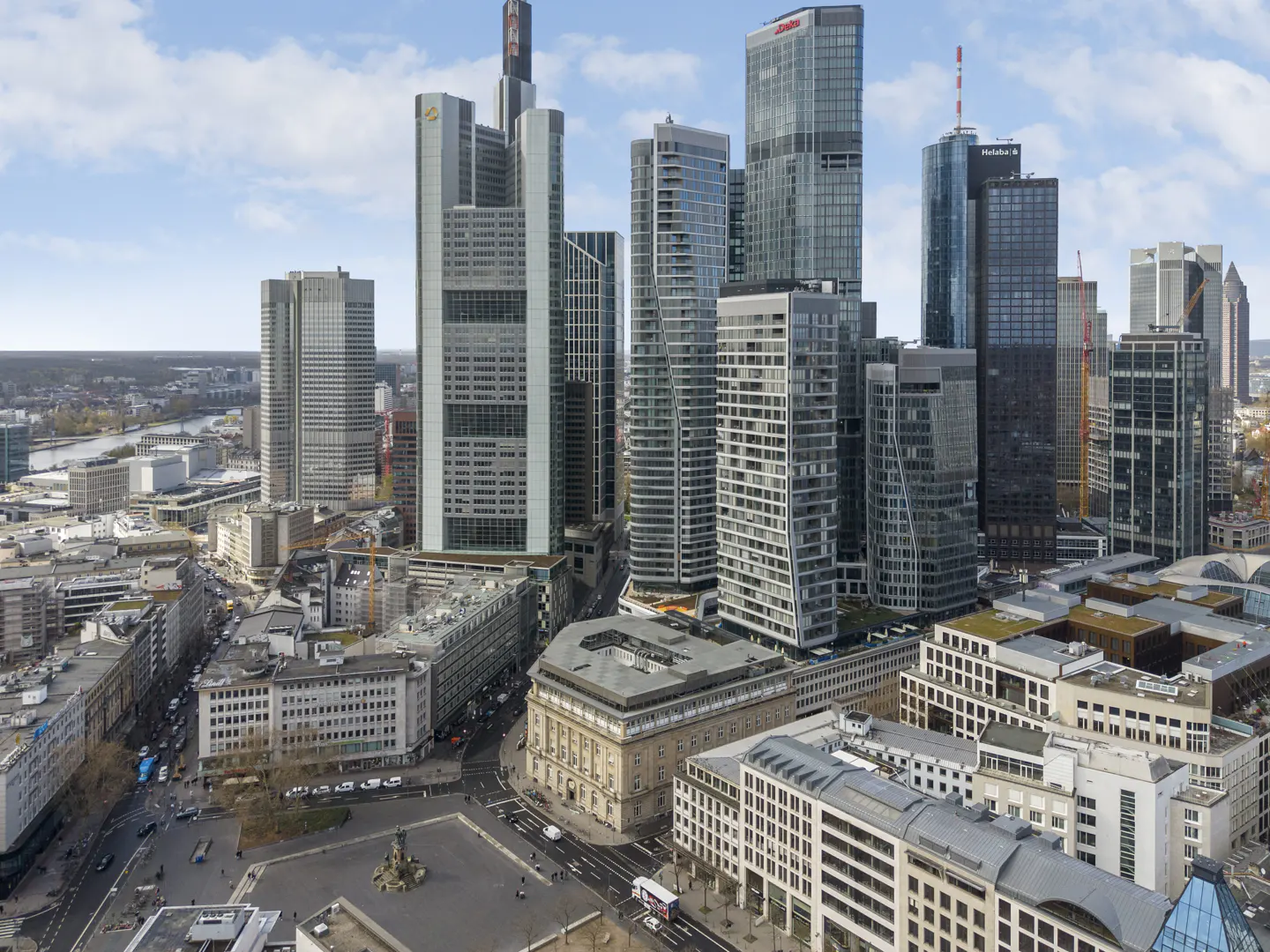 Aerial view of the Frankfurt skyline featuring modern glass skyscrapers, urban streets, and a central plaza under a blue sky.