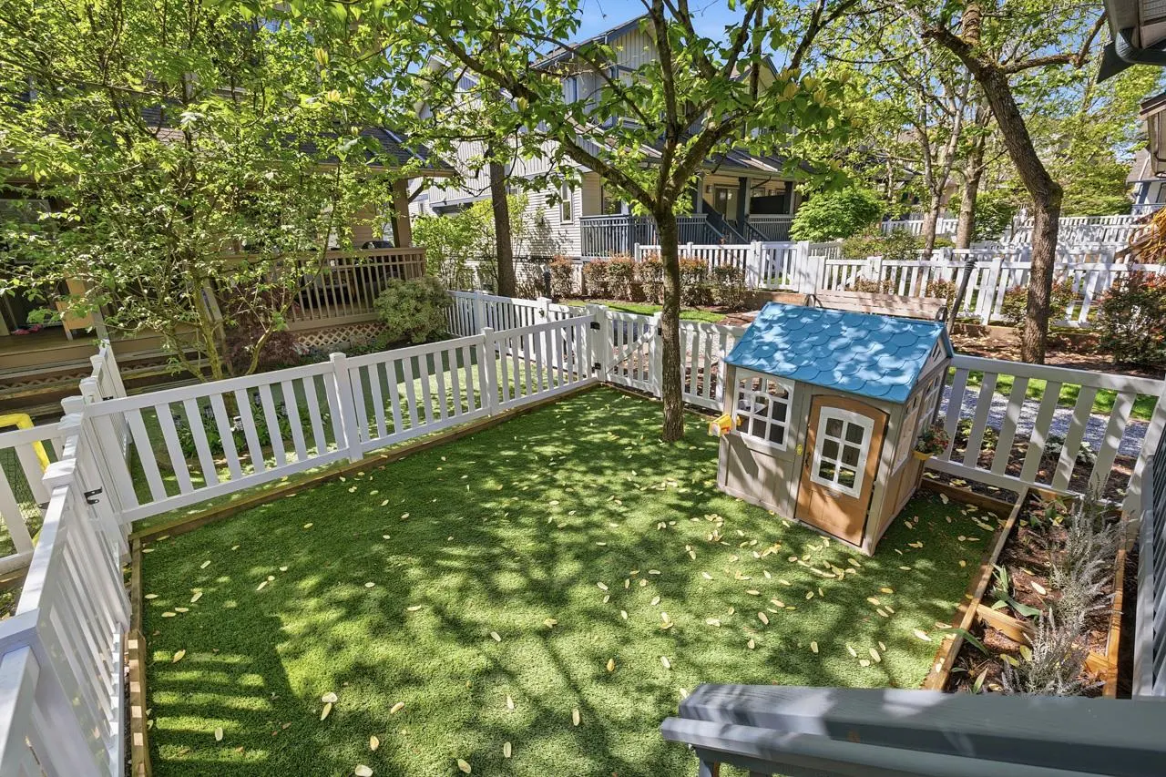 A backyard with green grass, a white picket fence, and a small playhouse with a blue roof.