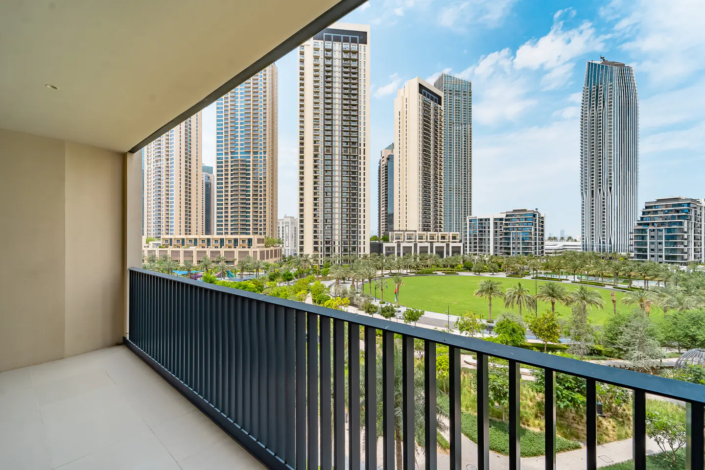 View from a balcony with black railings overlooking a green park and tall buildings in a city.