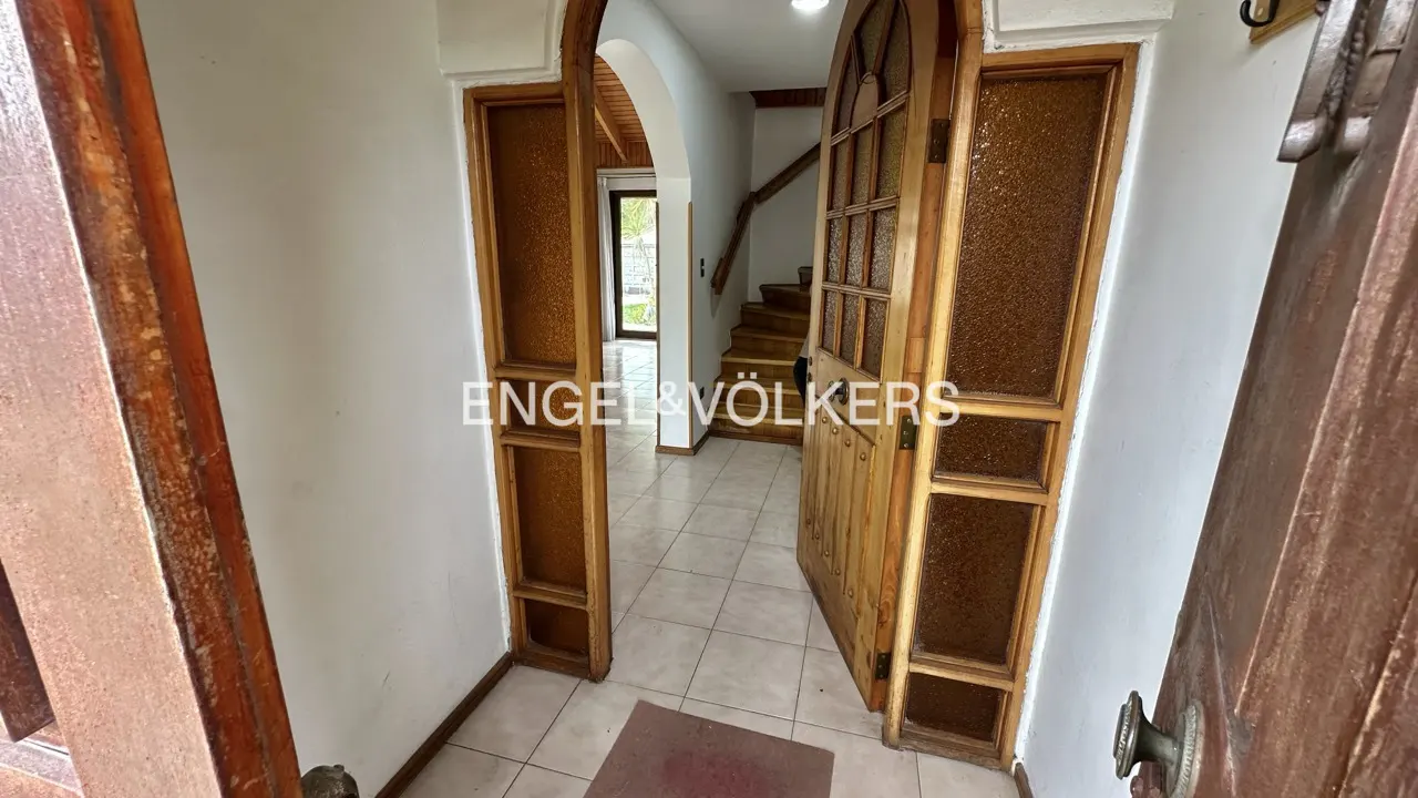 A view of the house's interior through an open wooden door, revealing a tiled floor, stairs, and the Engel & Völkers logo.