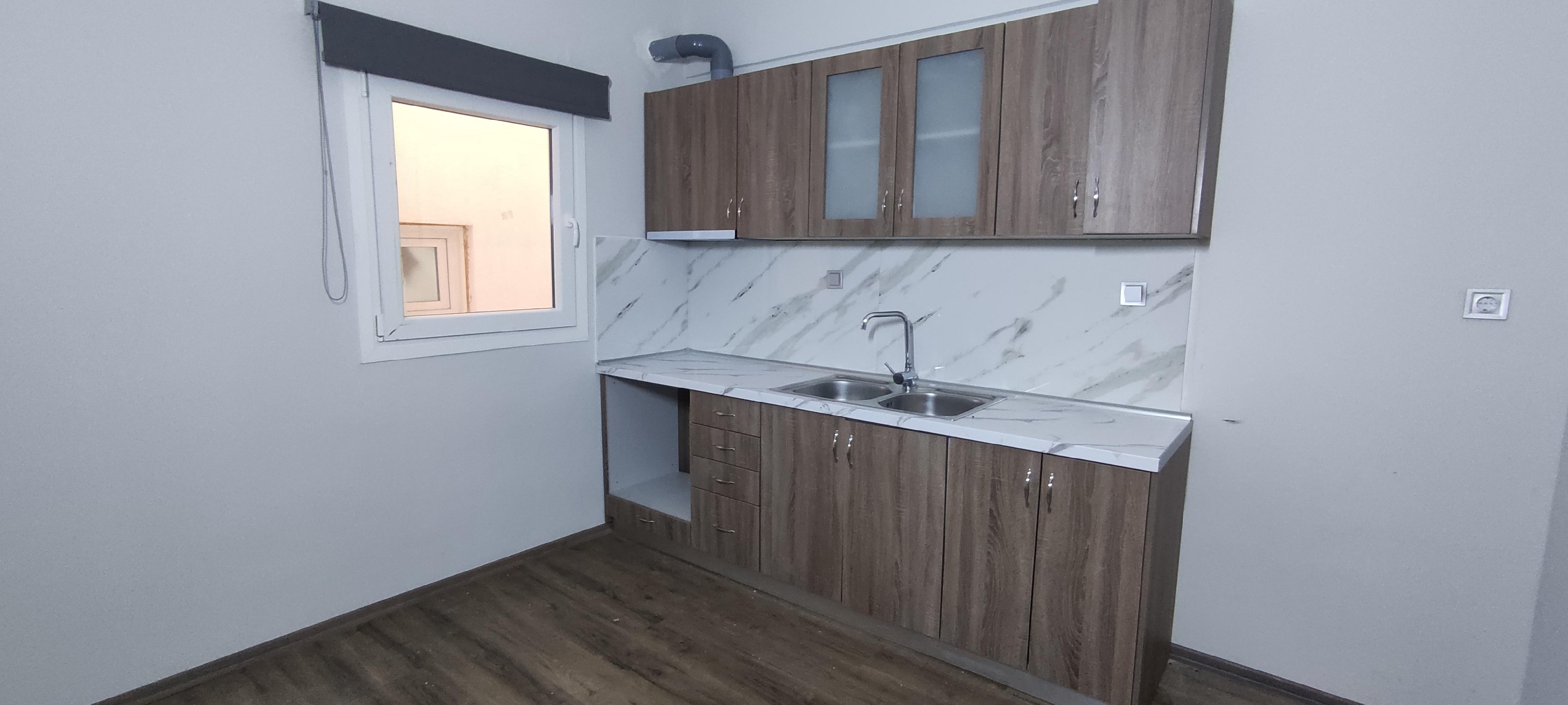 Modern kitchen with wood-grain cabinets, white marble-look backsplash, stainless steel sink, and a window with a blind.