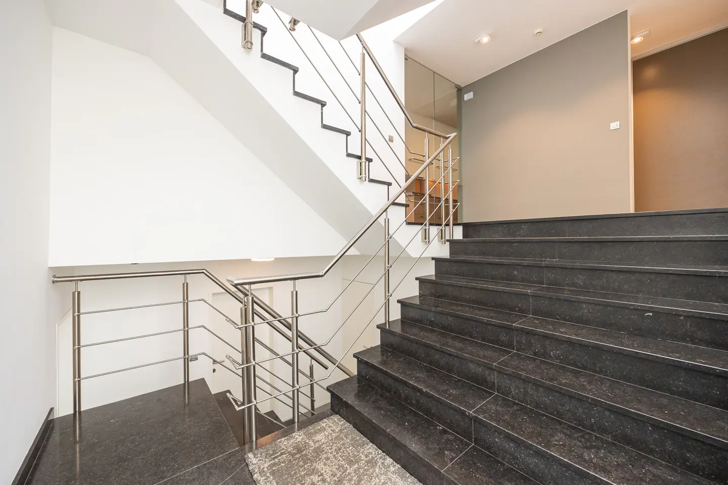 Interior view of a staircase with black marble steps and stainless steel railings in a modern building.
