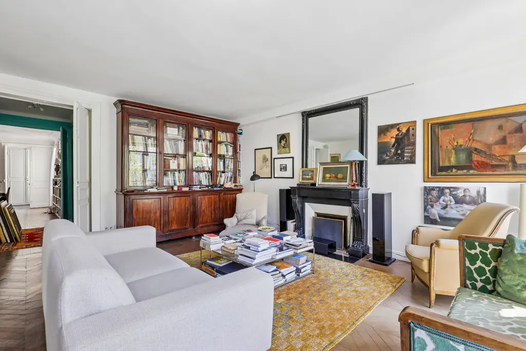 Bright living room with white sofa, wood bookcase, and black fireplace. Art hangs on the white walls, and a yellow rug covers the wood floor.