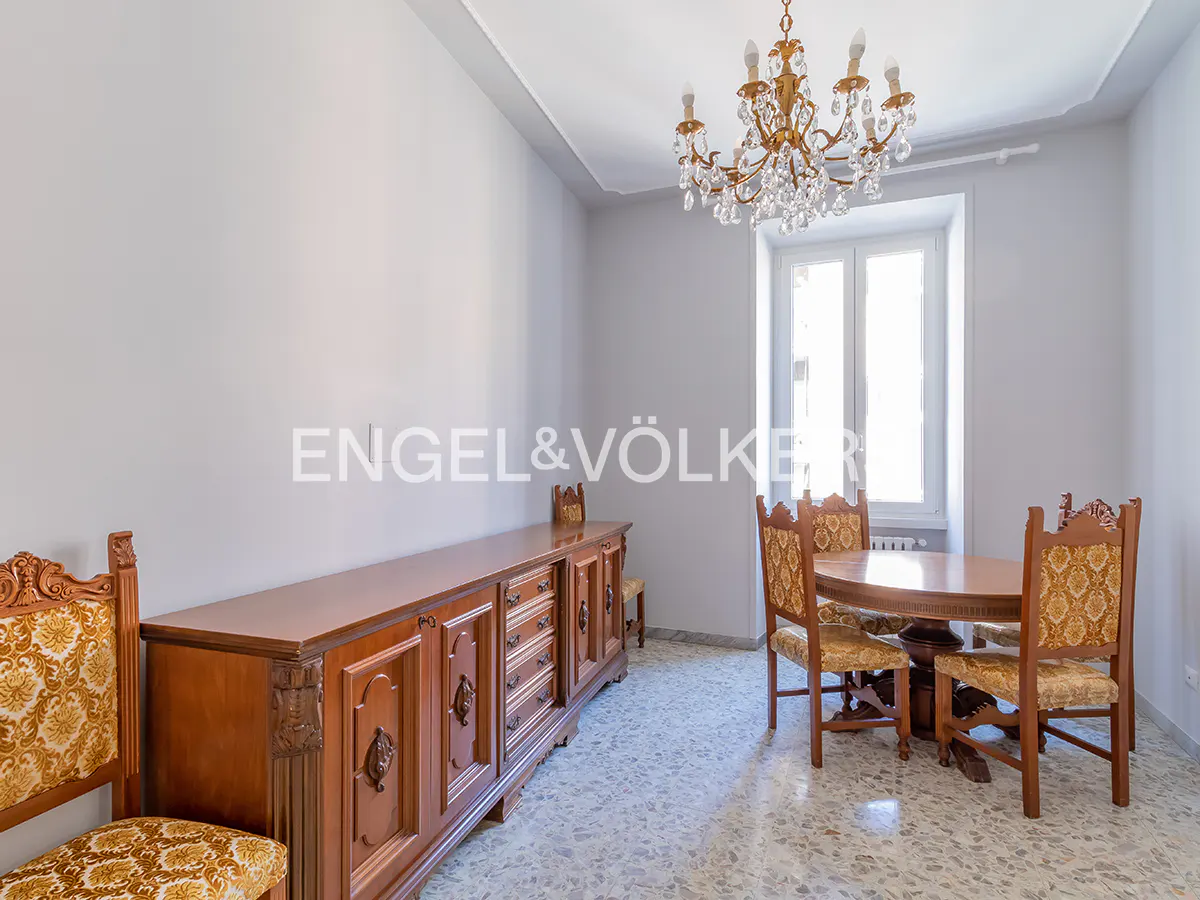 Dining room with a long wooden sideboard, a round table, and chairs with patterned gold upholstery under a crystal chandelier.