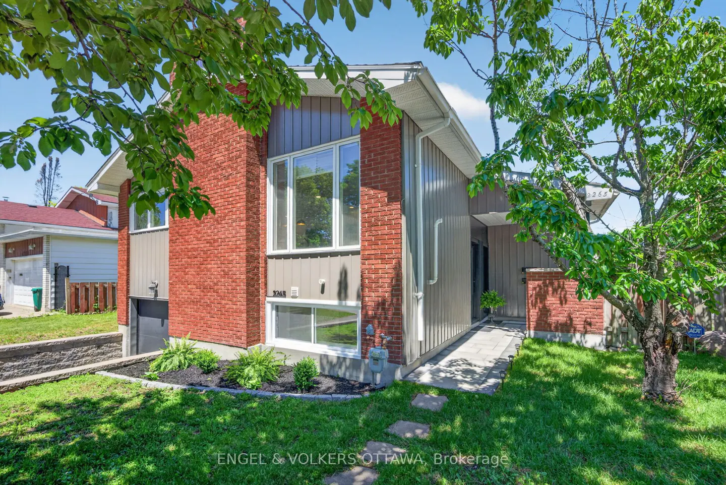 Exterior of a split-level home with red brick and grey vertical siding, a front lawn, and a stone walkway.