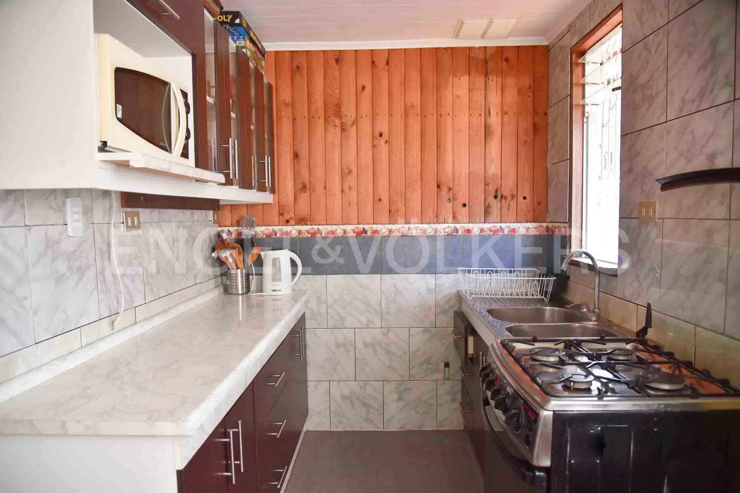 Kitchen with dark wood cabinets, white marble-look countertops, gas stove, and a wood-paneled accent wall.