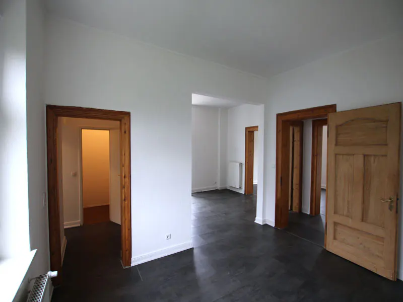 Empty room with white walls, dark floors, and wooden door frames. One door is open, revealing another room.