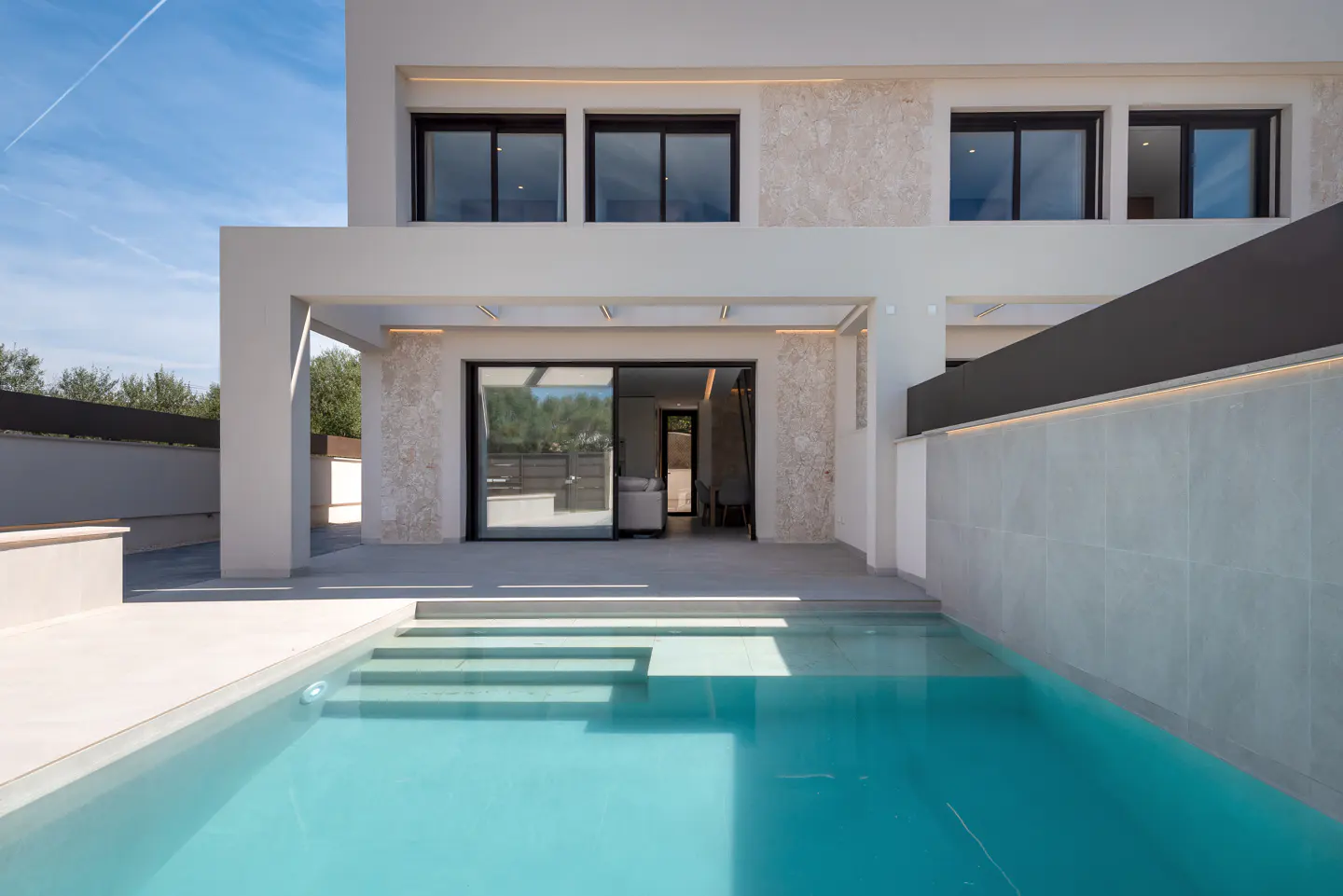 Modern white house with a turquoise pool in the foreground. The house has black framed windows and a sliding glass door.