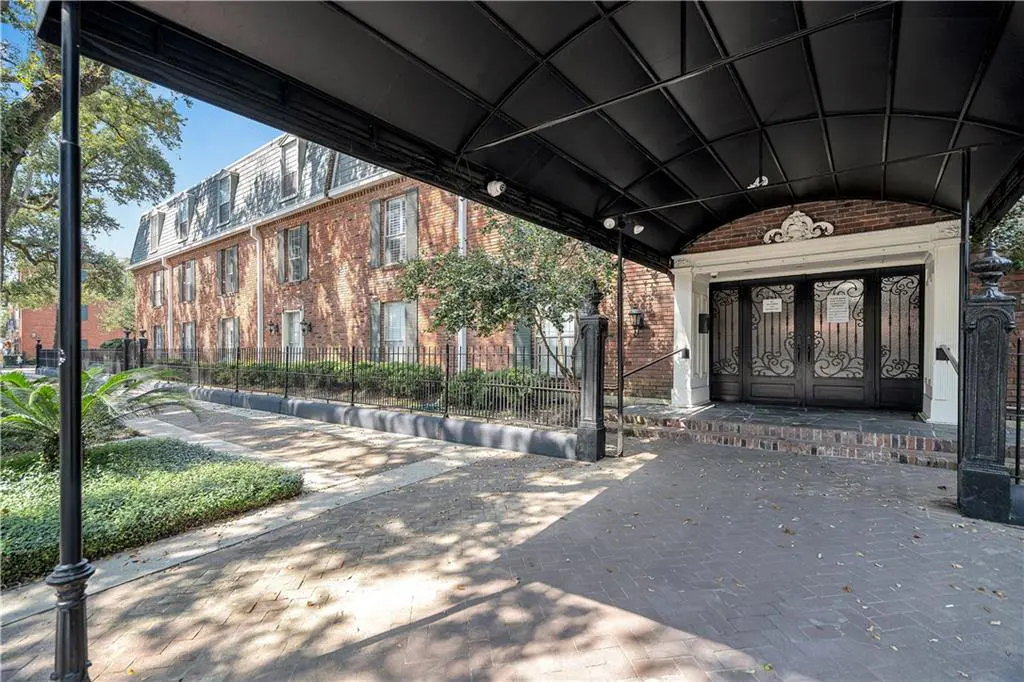 Exterior of a brick apartment building with a black metal awning over the entrance. A brick walkway leads to the ornate black doors.