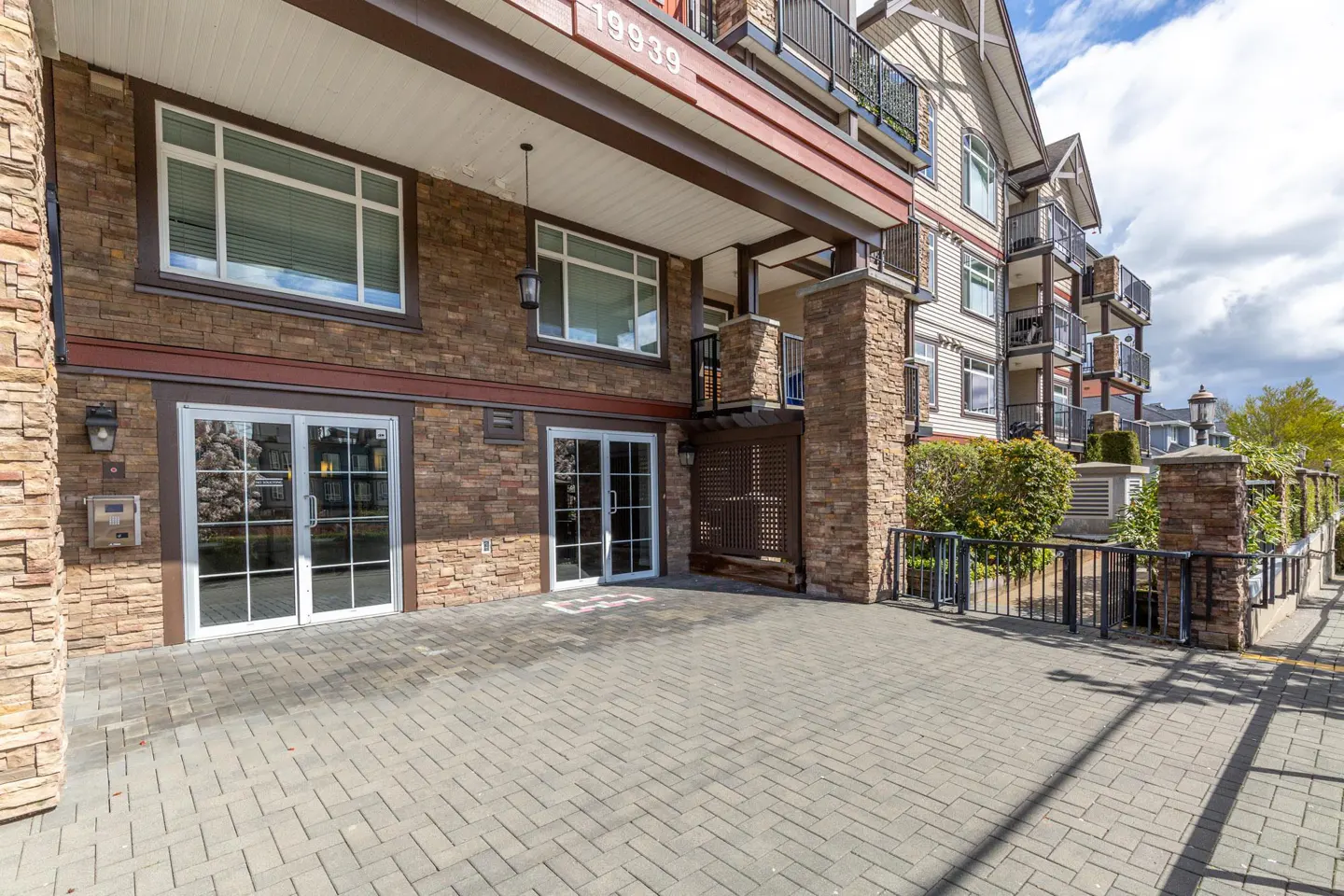 Exterior view of a multi-story apartment building with stone facade, white windows, and a paved entrance. Balconies with black railings are visible.