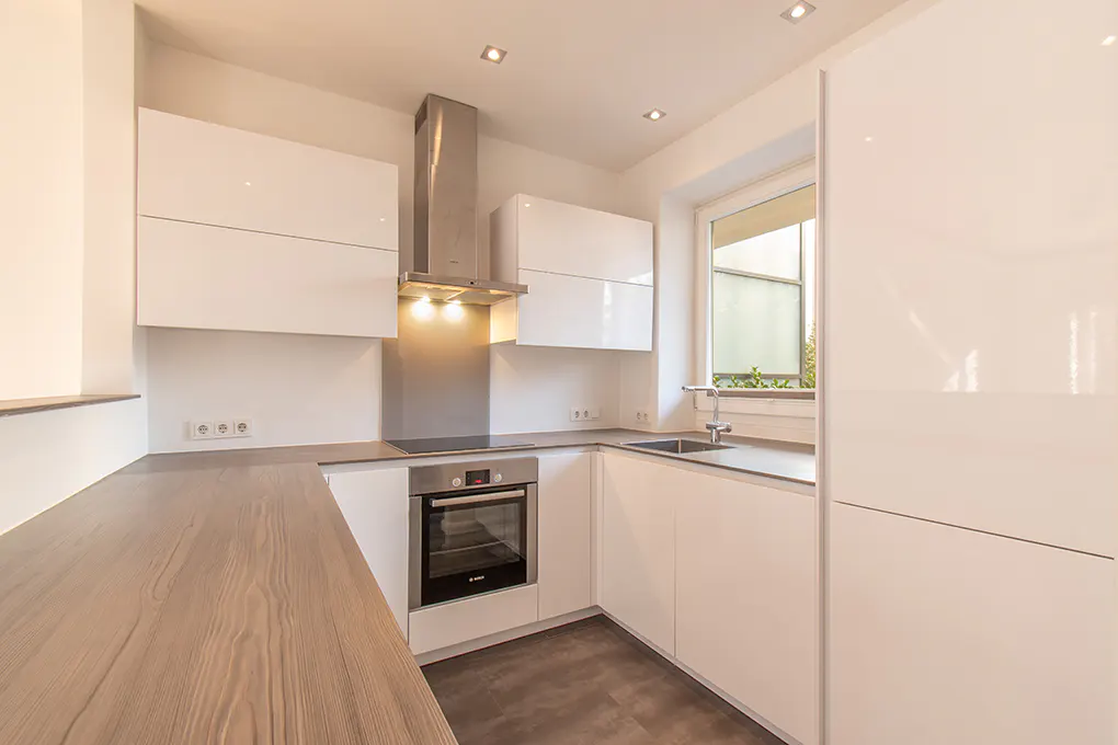 Bright, modern kitchen with white cabinets, stainless steel appliances, wood countertop, and a window.