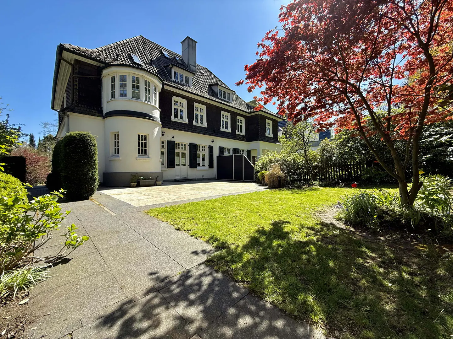 Exterior view of a two-story house with a green lawn, a red tree, and a stone walkway.