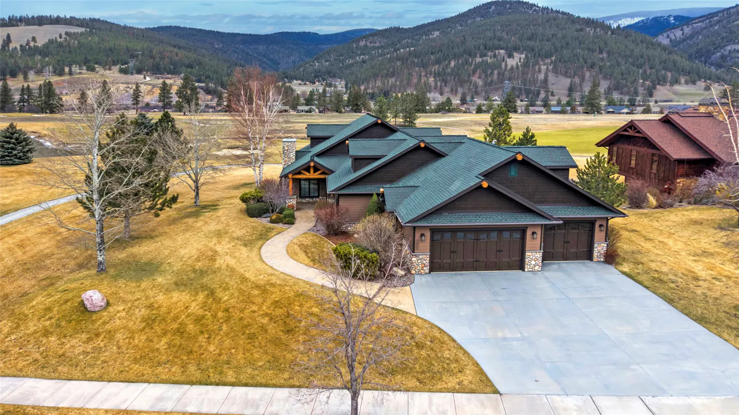 A brown house with a green roof and a three-car garage sits in front of a mountain range.