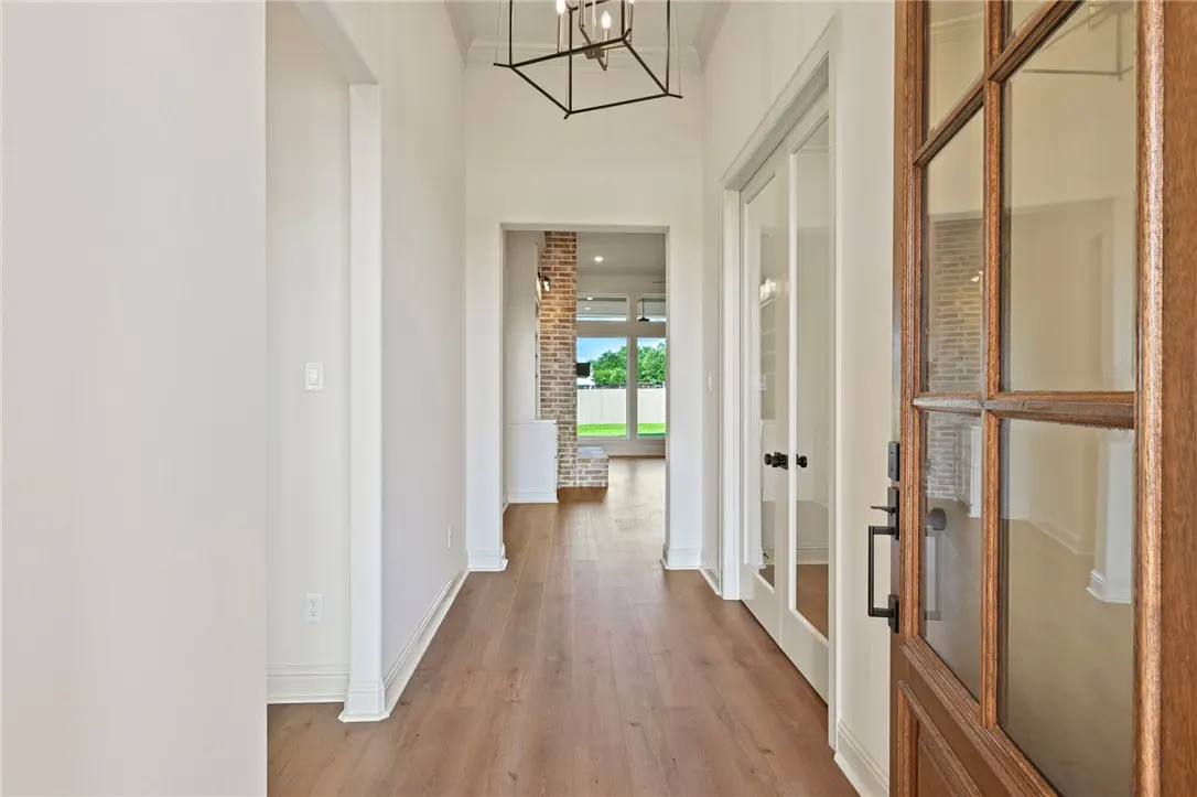 Bright hallway with wood floors, a modern geometric chandelier, and a view through to a brick fireplace and backyard.