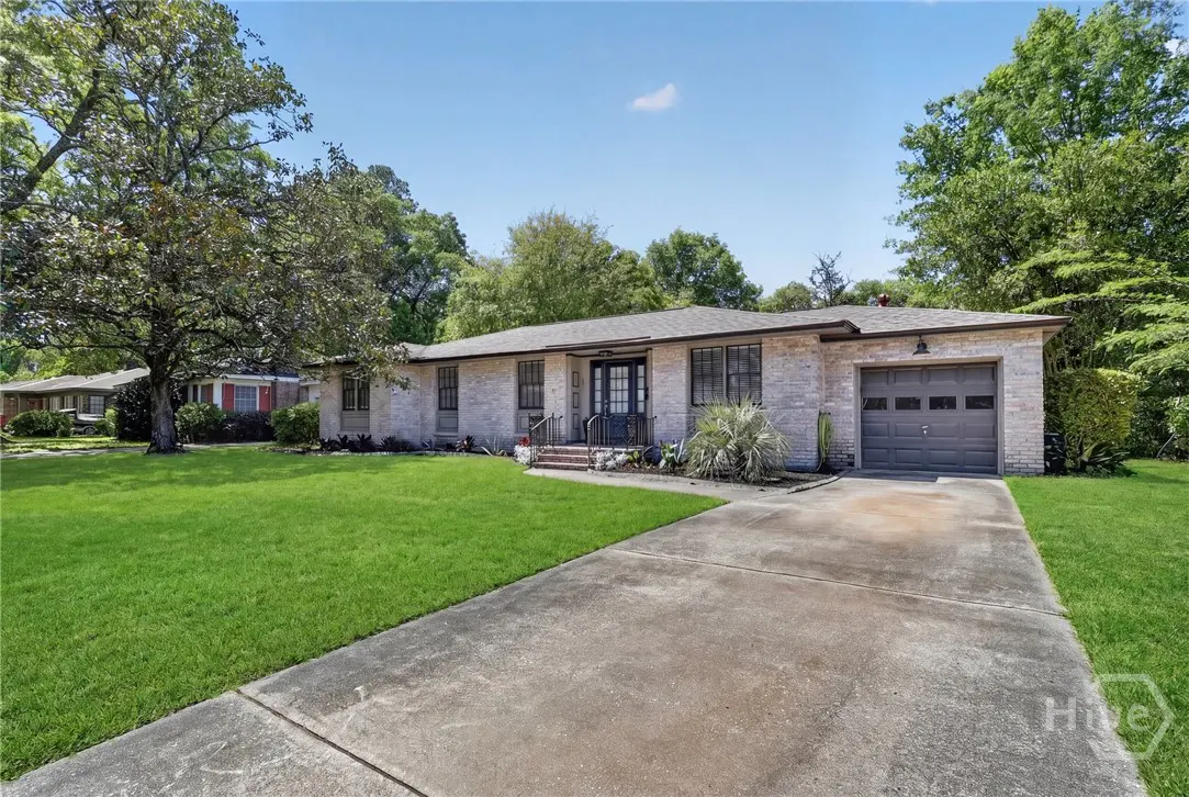 A single-story brick house with a gray roof, a two-car garage, and a green lawn on a sunny day.