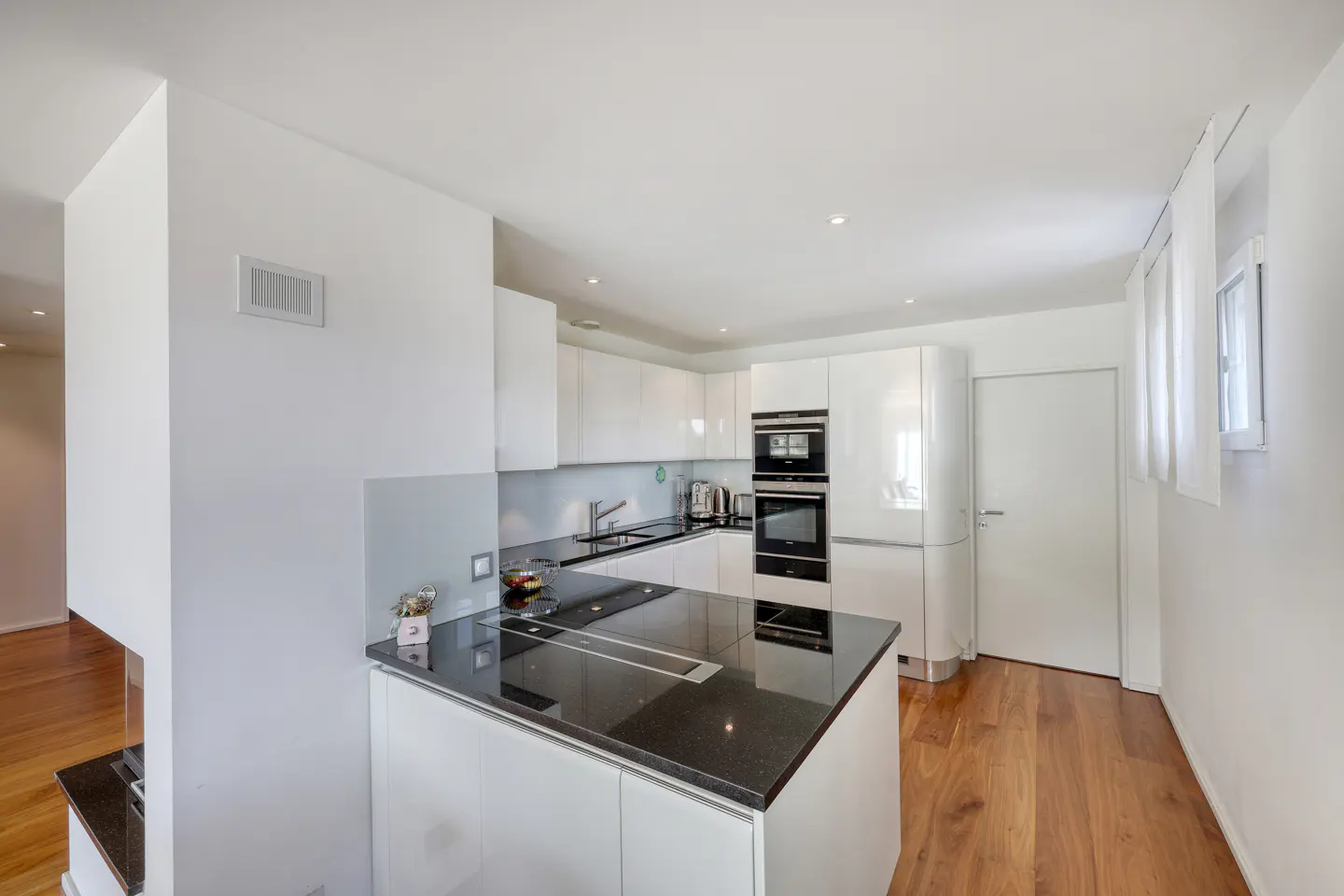 Bright kitchen with white cabinets, black countertops, and wood floors. Stainless steel appliances and a window with white blinds are visible.