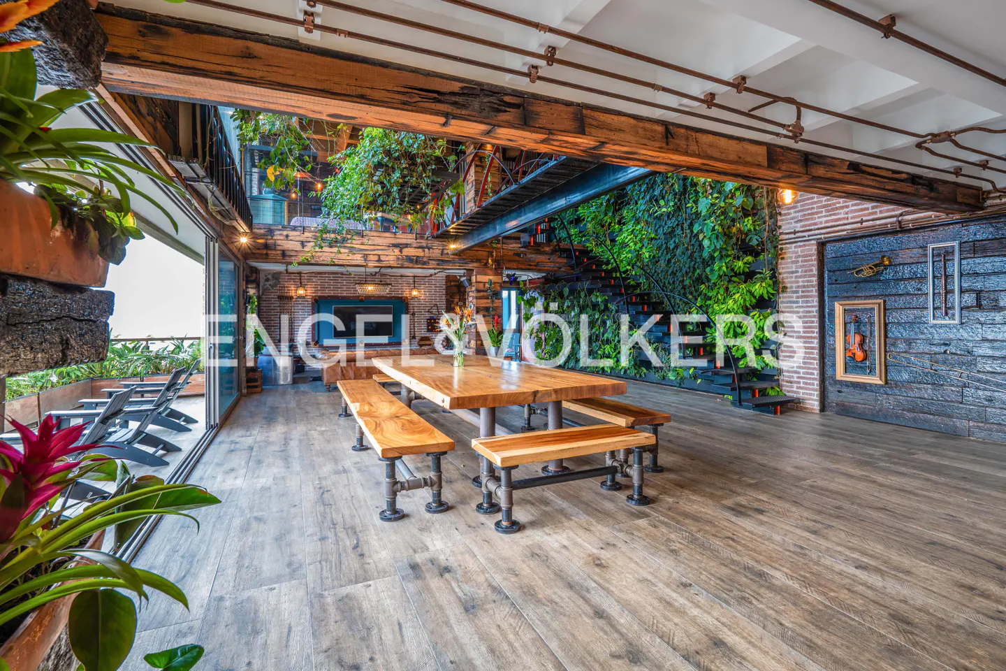 Indoor dining area with a wooden table and benches, brick walls, and a green wall with stairs.