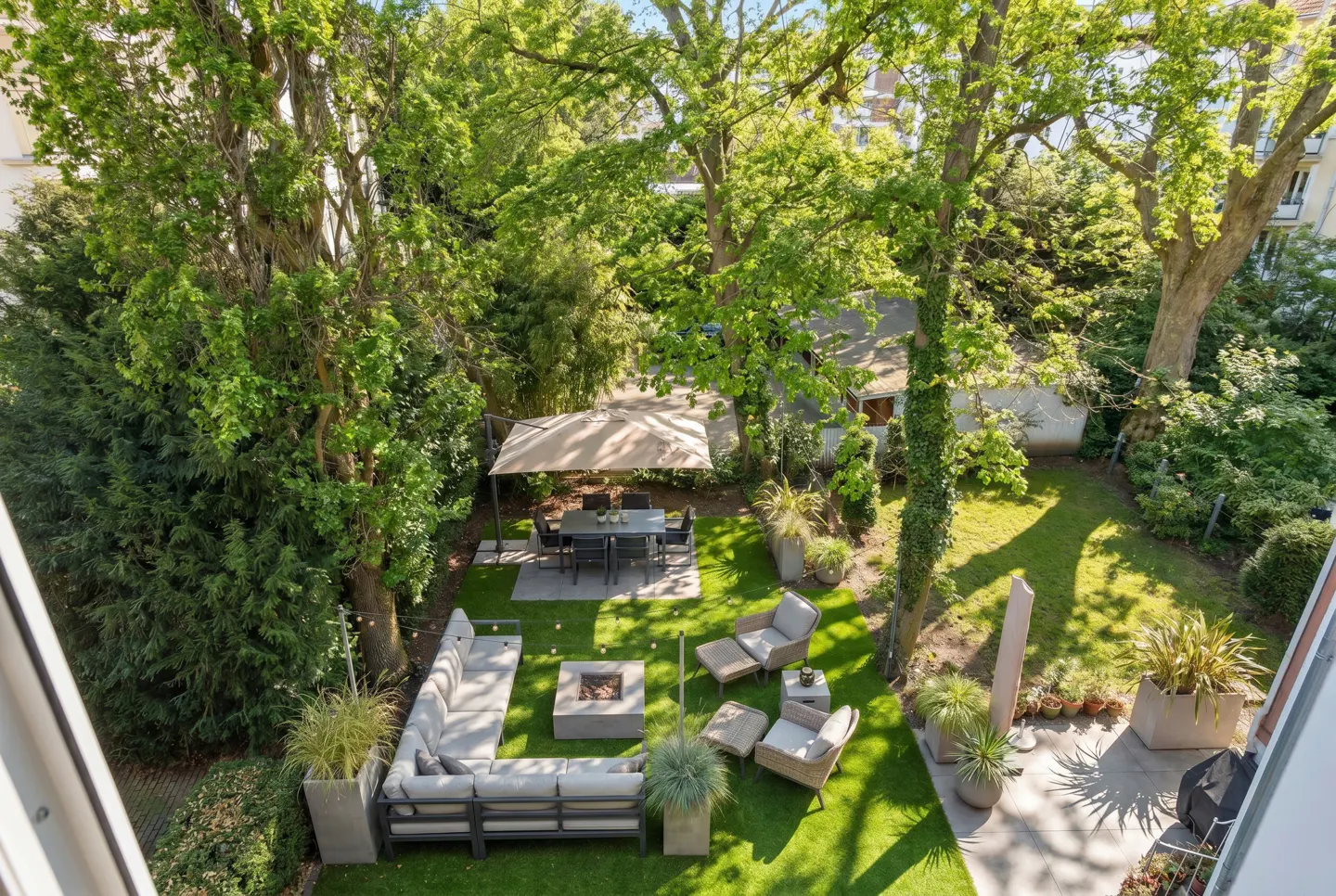 Overhead view of a green backyard with a patio set, lounge area with a fire pit, and lush trees.
