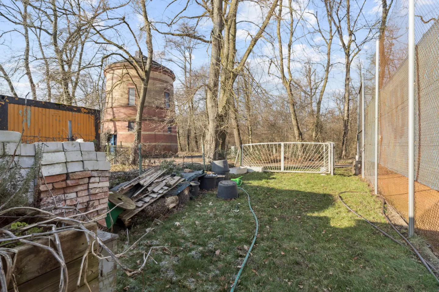 Overgrown backyard with a soccer goal, brick tower, and orange container in the background.