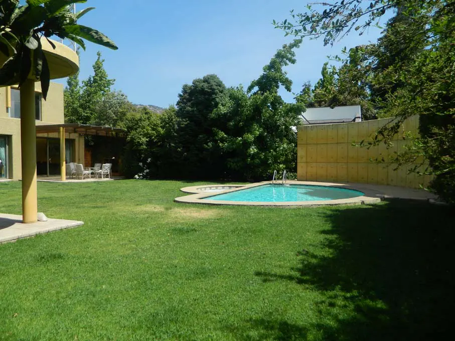 A backyard with a kidney-shaped pool, green lawn, and a yellow house with a patio and outdoor furniture.