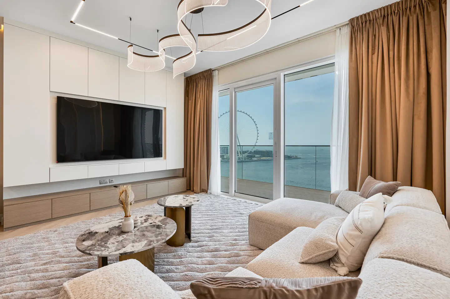 Living room with a large white sofa, marble tables, and a view of the ocean and Ferris wheel.