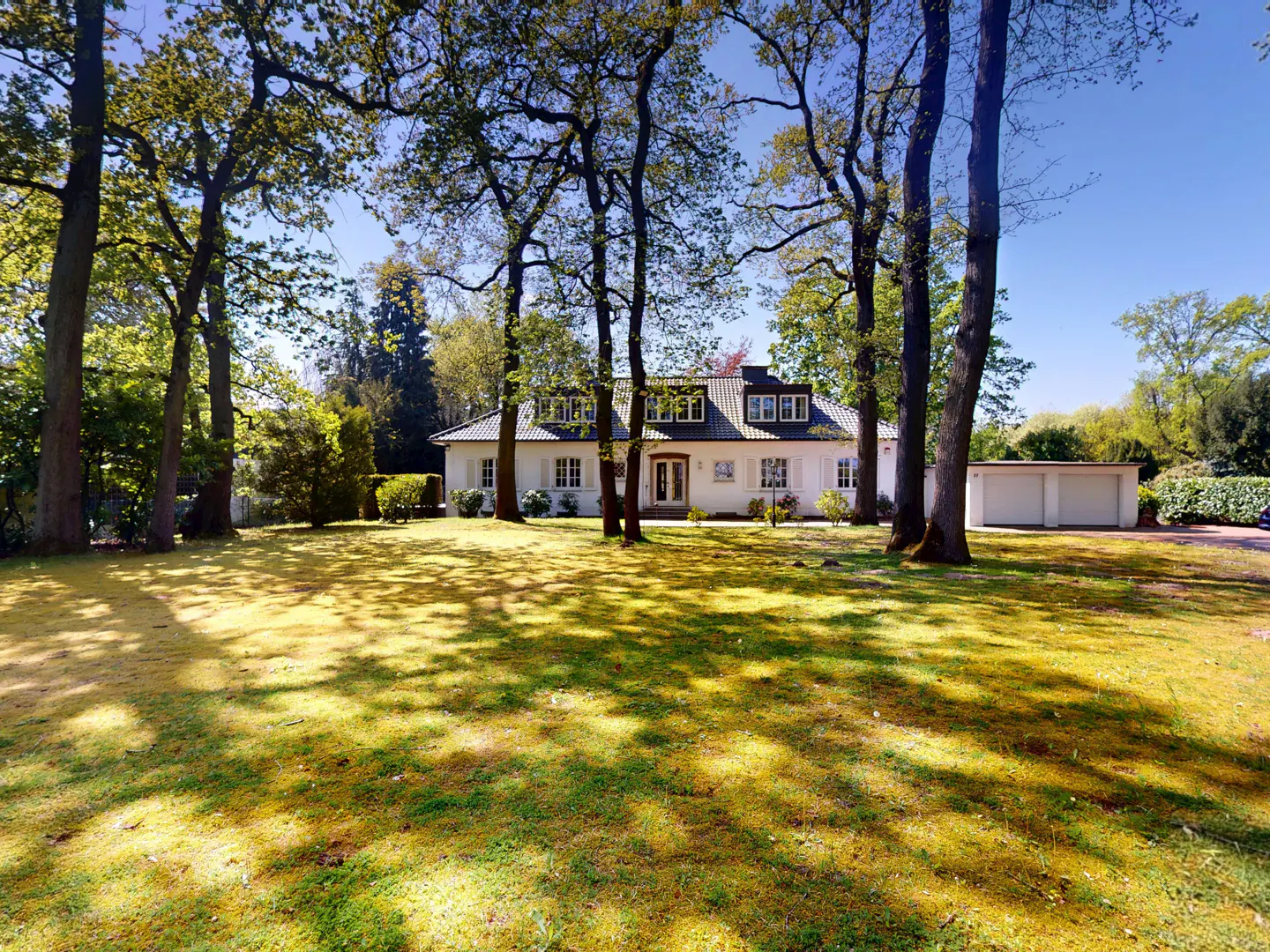 A white house with a gray roof is surrounded by trees and a green lawn.