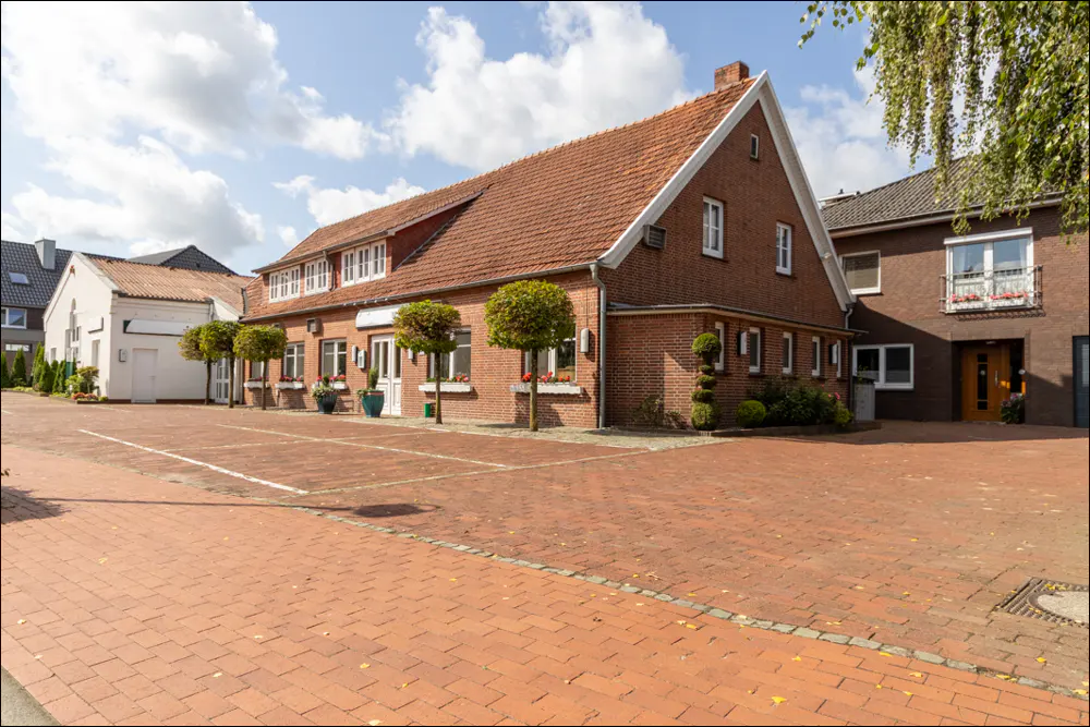A two-story brick building with a red tile roof and a brick parking lot.