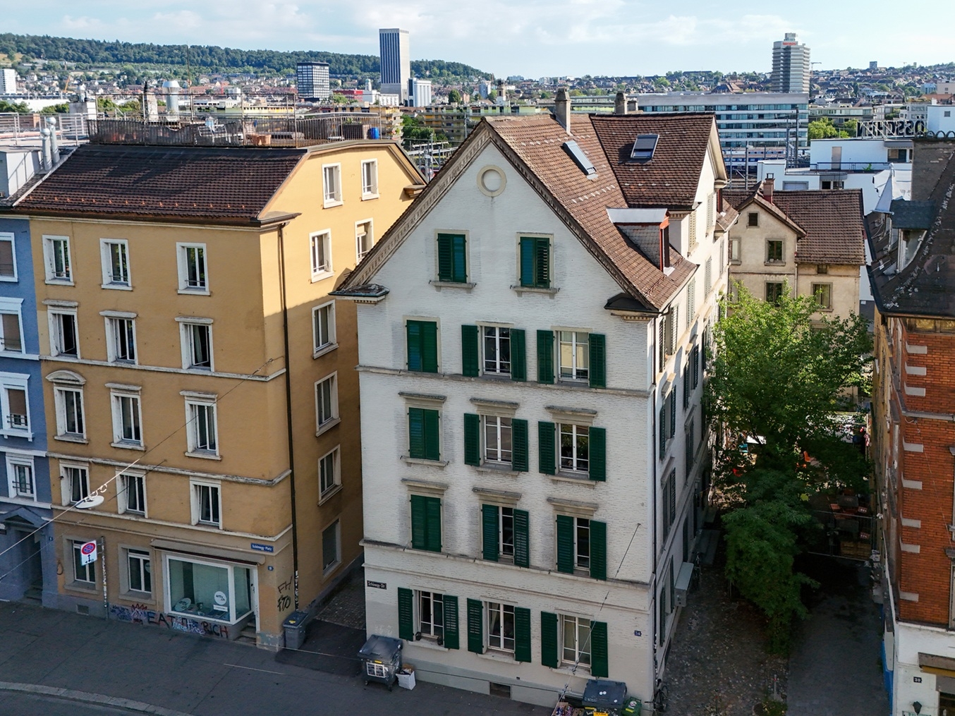 High-angle view of a white building with green shutters next to a yellow building in a dense urban city setting. [AI-generated text]
