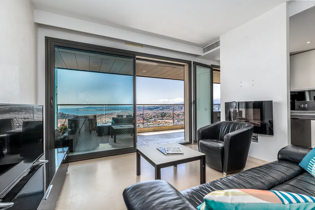 Living room with black leather furniture, a coffee table, and a large sliding glass door leading to a balcony with a city view.