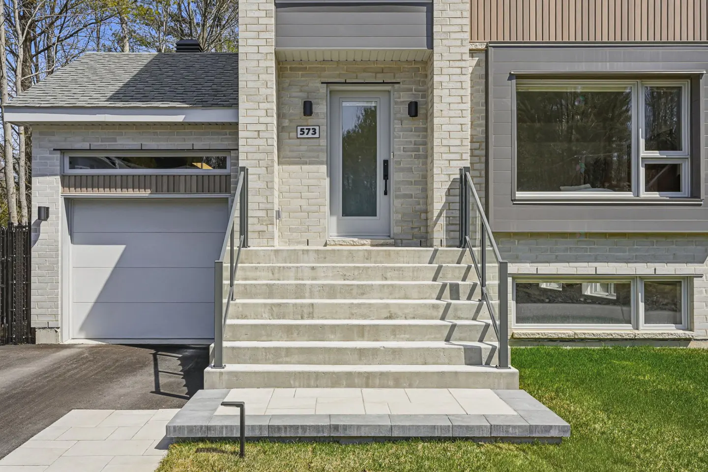 Exterior of a two-story house with brick, a white door, and concrete steps with metal railings. A garage is on the left.